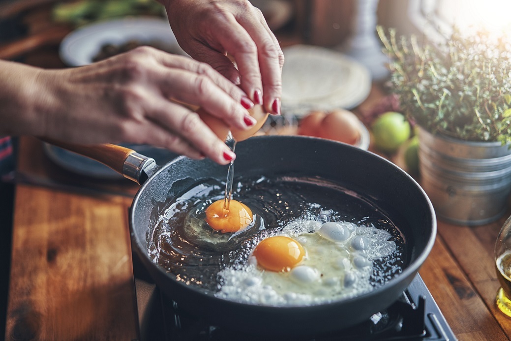 Hands cracking eggs into a skillet while making a keto-friendly breakfast